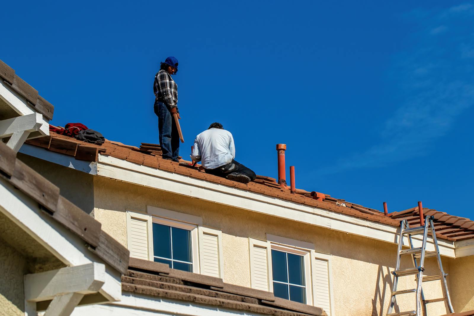 Roof construction scene with workers on a tiled roof, captured under a clear blue sky.