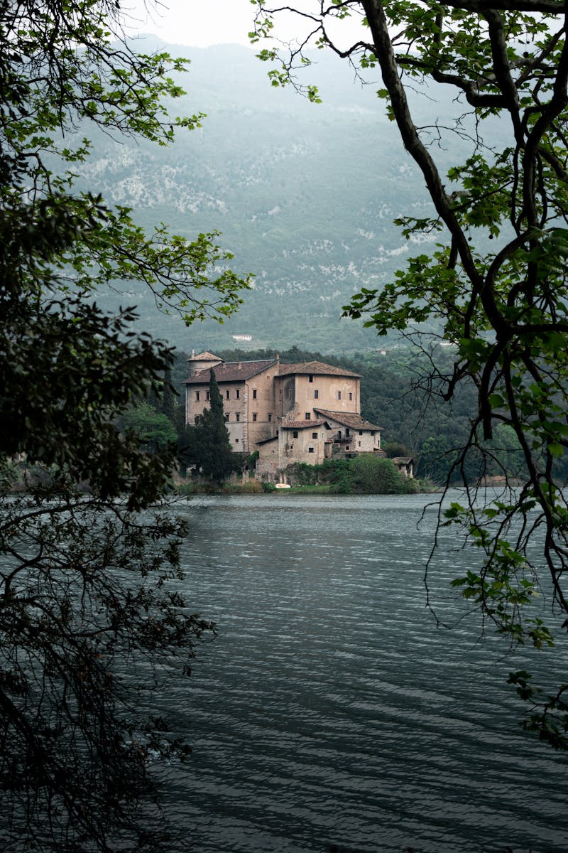 Tranquil view of Castle Toblino nestled by the lake in Arco, Italy, framed by trees.